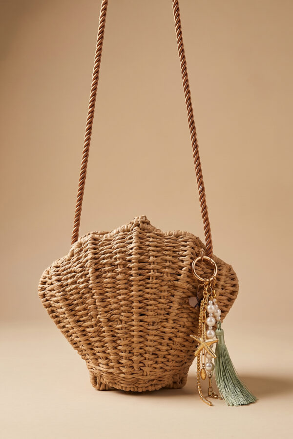 Bolso tejido Isla de Airavata en forma de concha, con correa al hombro y charms decorativos.